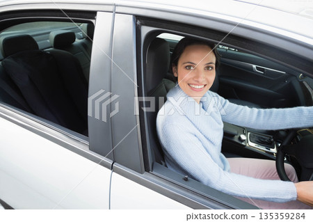 Female driver smiling and resting on steering wheel in white sedan with leather seats, copy space Female driver smiling and resting on steering wheel in white sedan with leather seats, copy space 135359284