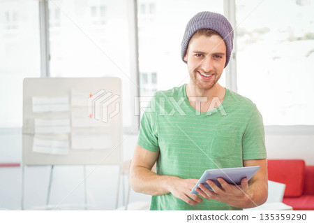 Man examining tablet while standing in coworking office near whiteboard and red sofa 135359290