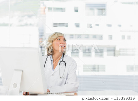 Female doctor wearing lab coat typing on keyboard at computer monitor with stethoscope at clinic Female doctor wearing lab coat typing on keyboard at computer monitor with stethoscope at clinic 135359339