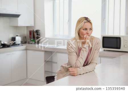 Woman in casual wear biting nails while leaning on white kitchen island, with papers, copy space Woman in casual wear biting nails while leaning on white kitchen island, with papers, copy space 135359340