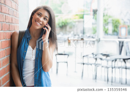African American woman leaning on brick wall using phone with backpack at cafe patio, copy space 135359346