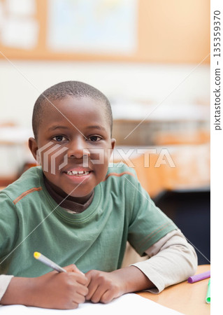 African American schoolboy writing on paper at wooden desk in classroom with yellow-tipped pencil 135359370