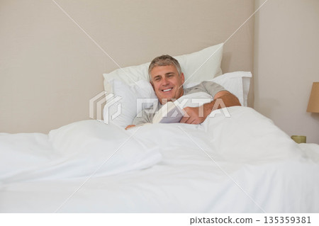 Man reading open book in bed in bedroom with pillows, lamp, ceramic mug, copy space Man reading open book in bed in bedroom with pillows, lamp, ceramic mug, copy space 135359381