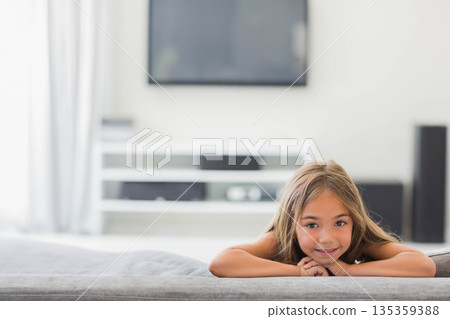 Child girl lying on gray sofa in living room with media console, TV, speaker, copy space Child girl lying on gray sofa in living room with media console, TV, speaker, copy space 135359388