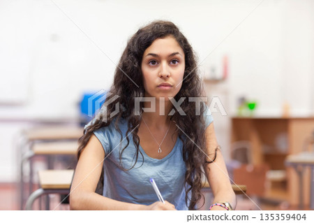 Female student writing notes while listening to instructor in classroom with pen and notebook Female student writing notes while listening to instructor in classroom with pen and notebook 135359404