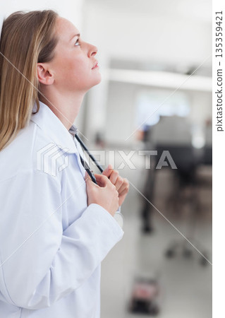 Female doctor holding stethoscope and looking upward in bright hospital corridor, copy space 135359421