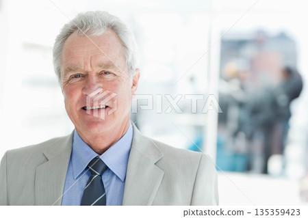 Senior businessman standing at reception in business attire by glass partitions, copy space 135359423