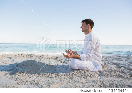 Adult man meditating cross-legged on sandy beach facing ocean horizon under clear sky, copy space Adult man meditating cross-legged on sandy beach facing ocean horizon under clear sky, copy space 135359434