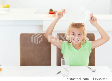 Child girl raising empty plate above head while sitting at kitchen table with water glass Child girl raising empty plate above head while sitting at kitchen table with water glass 135359450