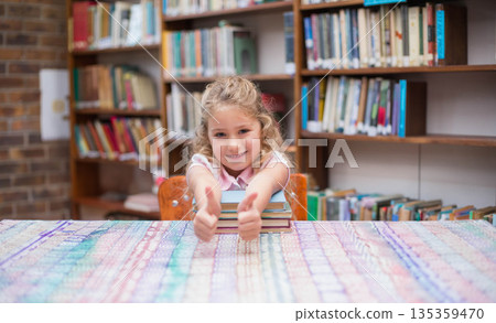 Female child student leaning on stacked books on patterned tablecloth in library giving thumbs up Female child student leaning on stacked books on patterned tablecloth in library giving thumbs up 135359470