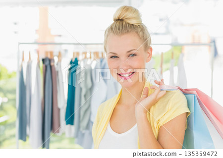 Female shopper smiling and holding pastel shopping bags on shoulder in bright shop, copy space 135359472