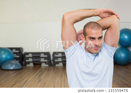 Man performing triceps stretch in gym studio with stability balls and step platforms, copy space Man performing triceps stretch in gym studio with stability balls and step platforms, copy space 135359478