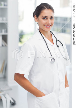 Hispanic female doctor standing and smiling in clinic wearing white lab coat with stethoscope 135359489