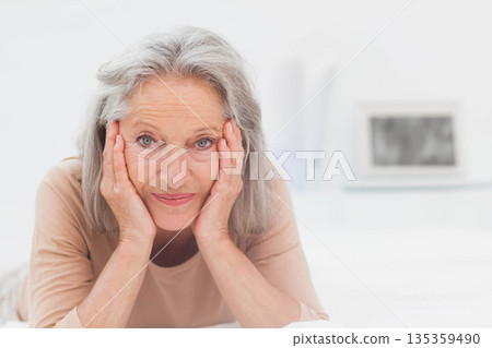 Senior woman lying on bed in bedroom, leaning on hands among books and focusing on laptop 135359490