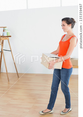 Woman holding cardboard box while standing in bright art studio with wooden easel, copy space Woman holding cardboard box while standing in bright art studio with wooden easel, copy space 135359497