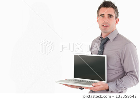 Male in grey shirt and tie standing against white studio backdrop holding silver laptop, copy space Male in grey shirt and tie standing against white studio backdrop holding silver laptop, copy space 135359542