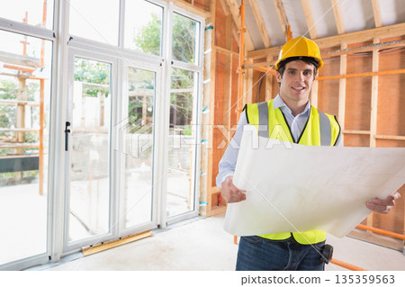 Male builder standing by sliding glass doors holding plans in hard hat, copy space Male builder standing by sliding glass doors holding plans in hard hat, copy space 135359563