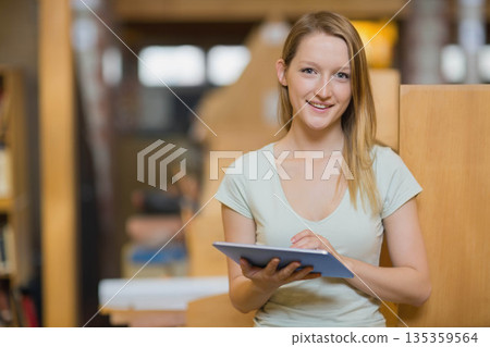 Woman studying in library tapping tablet screen by wooden study carrels and bookshelves, copy space Woman studying in library tapping tablet screen by wooden study carrels and bookshelves, copy space 135359564