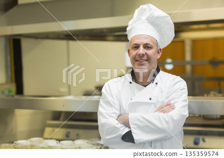 Mid adult male chef wearing white jacket standing in professional kitchen by stainless steel range Mid adult male chef wearing white jacket standing in professional kitchen by stainless steel range 135359574