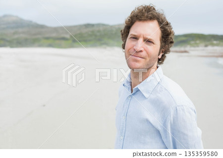 Middle-aged man standing on coastal beach overlooking distant hills and calm shoreline, copy space Middle-aged man standing on coastal beach overlooking distant hills and calm shoreline, copy space 135359580