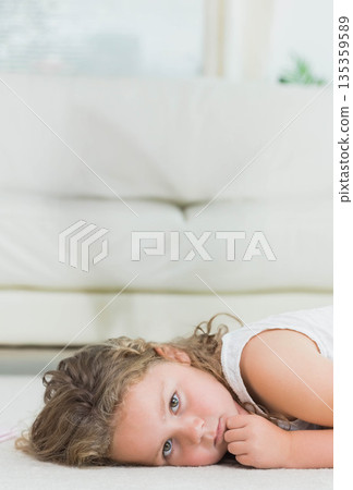 Girl resting on carpet under window in living room with white sofa and potted plant Girl resting on carpet under window in living room with white sofa and potted plant 135359589