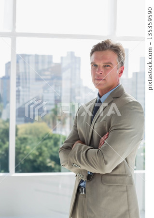 Man wearing suit jacket standing near window wall in lobby overlooking city skyline, copy space 135359590