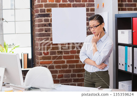 Mid-adult Chinese woman standing at desk in office using computer monitor and mouse, copy space 135359624