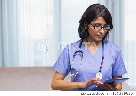 Female nurse wearing scrubs holding tablet and stethoscope by exam bed in exam room, copy space Female nurse wearing scrubs holding tablet and stethoscope by exam bed in exam room, copy space 135359650