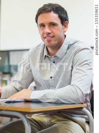 Male trainee wearing gray shirt writing in spiral notebook with pen at classroom desk 135359651