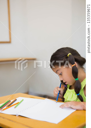 Schoolgirl drawing in notebook with colored pencils at school desk wearing green top, copy space 135359671