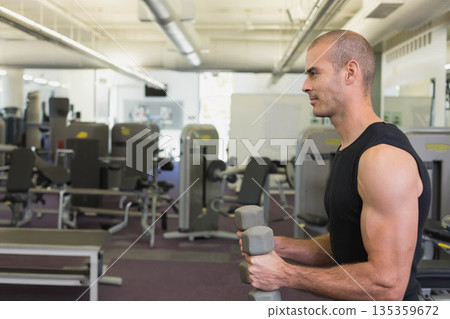 Man holding grey dumbbells in gym with weight machines mirrored wall ventilation ducts, copy space 135359672