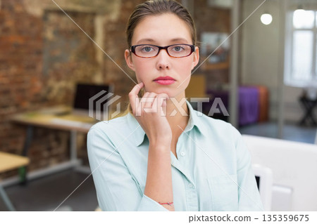 Woman sitting at desk in office wearing glasses, green shirt using laptop near glass partition Woman sitting at desk in office wearing glasses, green shirt using laptop near glass partition 135359675