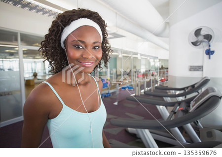 African American woman standing by treadmills in gym wearing sweatband and earphones, copy space 135359676