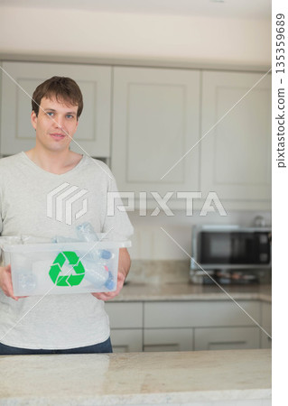 Man in his thirties holding recycling bin full of bottles on countertop, copy space 135359689