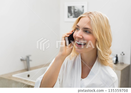 Woman standing at bathroom vanity wearing bathrobe talking on smartphone near sink, copy space Woman standing at bathroom vanity wearing bathrobe talking on smartphone near sink, copy space 135359708