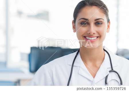 Smiling female doctor wearing lab coat and stethoscope in clinic with computer monitors, copy space Smiling female doctor wearing lab coat and stethoscope in clinic with computer monitors, copy space 135359726