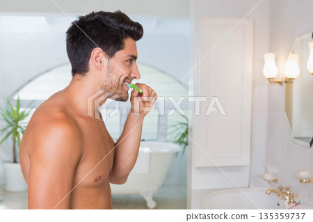 Man brushing teeth at bathroom sink using green toothbrush near mirror and bathtub 135359737