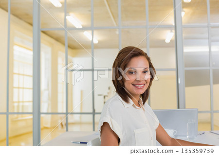 Hispanic woman wearing blouse typing on laptop with notebook, pen and water glass at office desk Hispanic woman wearing blouse typing on laptop with notebook, pen and water glass at office desk 135359739