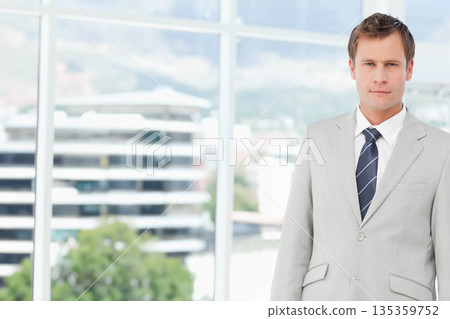 Mid adult man wearing suit jacket with striped tie standing in office by windows, copy space 135359752