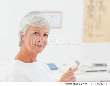 Senior female clinician holding stethoscope in exam room with skeleton chart, copy space Senior female clinician holding stethoscope in exam room with skeleton chart, copy space 135359754