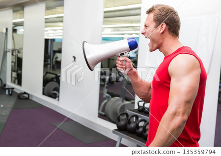 Man standing in gym weight area holding megaphone, shouting near kettlebells dumbbells, copy space Man standing in gym weight area holding megaphone, shouting near kettlebells dumbbells, copy space 135359794