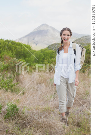 woman walking on hillside with backpack wearing cargo pants and hiking boots, copy space 135359795