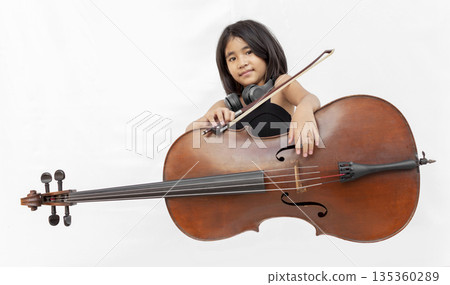 Asian girl in black dress playing cello and shouting with headphone. Concept for music education, child prodigy, emotional performance, and creative talent Asian girl in black dress playing cello and shouting with headphone. Concept for music education, child prodigy, emotional performance, and creative talent 135360289