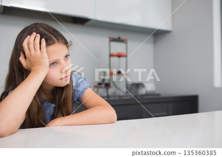 Female child leaning on hand and gazing right at kitchen countertop with dish rack, copy space 135360385