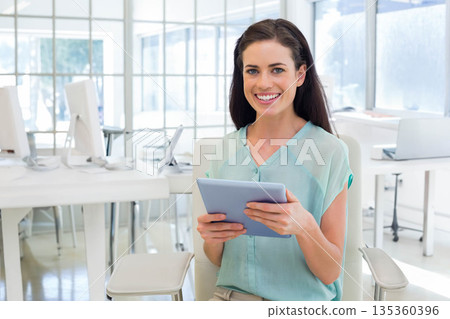 Woman holding tablet in both hands and smiling in open-plan office with white desks and computers 135360396
