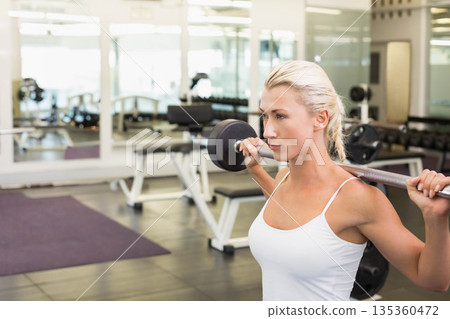 Woman in workout clothes holding loaded barbell in gym free weights section with mirror, copy space Woman in workout clothes holding loaded barbell in gym free weights section with mirror, copy space 135360472