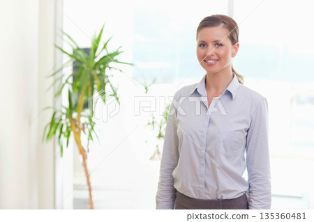 Woman standing by potted plant near large window wearing blue shirt in bright office, copy space Woman standing by potted plant near large window wearing blue shirt in bright office, copy space 135360481