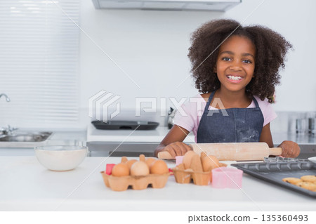 African American girl in denim apron rolling dough with rolling pin on kitchen counter, copy space African American girl in denim apron rolling dough with rolling pin on kitchen counter, copy space 135360493