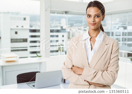 Female business professional standing with arms crossed in office by desk laptop papers, copy space Female business professional standing with arms crossed in office by desk laptop papers, copy space 135360511