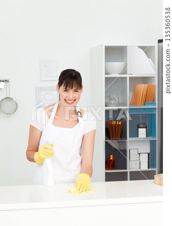 Mid adult woman cleaning countertop in kitchen wearing yellow gloves using spray bottle with cloth Mid adult woman cleaning countertop in kitchen wearing yellow gloves using spray bottle with cloth 135360538